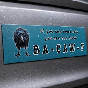 May include: A rectangular teal bumper sticker featuring a black crow illustration on the left side. The text reads, "If you can read this you are too close" in a simple font, followed by the large, bold, white-outlined text "BA-CAW-F" below it.