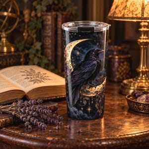 May include: A cylindrical tumbler with a clear lid featuring a dark blue and black night sky design. The graphic depicts a large, detailed black raven perched on a golden crescent moon surrounded by small stars, constellations, and floral accents.