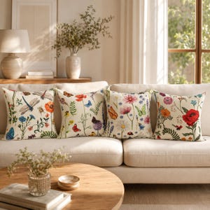 Op de afbeelding: Vier decoratieve kussens met bloemen- en insectenontwerpen. Elk kussen heeft een ander patroon van bloemen, vlinders en libellen in verschillende kleuren op een crèmekleurige achtergrond.
