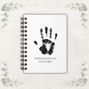 Puede incluir: Un cuaderno blanco con espiral con una huella de mano negra y las palabras "EXPERIENTIAL RECORD" impresas debajo. El cuaderno está rodeado de ramitas decorativas de hojas verdes y grises.