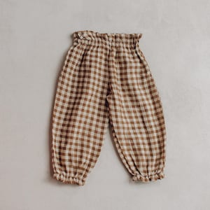 May include: Brown and white gingham trousers featuring a high-waisted design with a ruffled elastic waistband and matching ruffled elastic cuffs at the ankles. The trousers have a relaxed, loose-fitting silhouette throughout the legs.