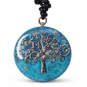 Peut inclure: Un collier pendentif rond avec un motif d'arbre argenté sur un fond bleu et turquoise. Le pendentif est suspendu à un cordon noir. Le motif de l'arbre est détaillé et complexe, avec un aspect texturé et scintillant.