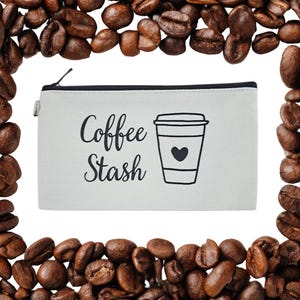 May include: An off-white canvas pouch with a black zip, displaying the words "Coffee Stash" and a coffee cup graphic with a heart. The pouch is framed by a border of roasted coffee beans.