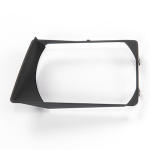 May include: A matte black rectangular plastic frame with a wide, angled side panel. The structure features a hollow center and thin, rigid edges, designed with a tapered profile that extends outward on one side, creating a distinct geometric shape.
