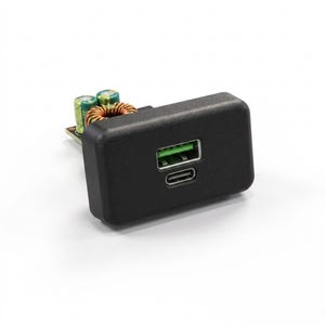 Może przedstawiać: Czarny, prostokątny moduł elektroniczny z przednim portem USB-A z zielonym wnętrzem oraz portem USB-C poniżej. Tylna część urządzenia odsłania płytkę drukowaną z dwoma zielonymi cylindrycznymi kondensatorami i cewką z drutu miedzianego.