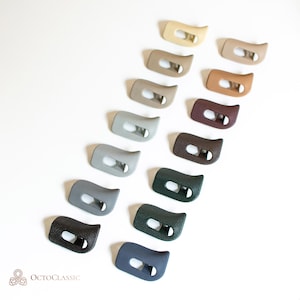 Op de afbeelding: Een verzameling auto-interieur trimstukken in verschillende kleuren, waaronder beige, grijs, bruin en zwart. Elk stuk heeft een gebogen vorm met een rechthoekige opening. Het OctoClassic-logo is linksonder zichtbaar.