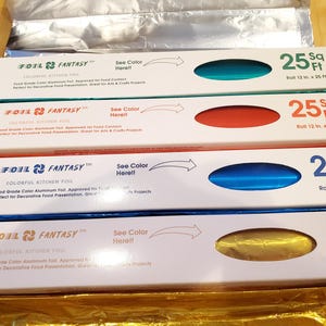 May include: Four rectangular boxes of Foil Fantasy colourful kitchen foil, each measuring 30.48 cm by 7.62 metres. The boxes feature a cutout window displaying teal, red, blue, and gold aluminium foil, with text indicating 25 Sq Ft per roll.