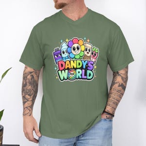 May include: An olive green V-neck t-shirt featuring a colorful graphic print with the text DANDY'S WORLD. The design includes several cartoon characters, including a multi-colored flower, a blue figure, and a pink character, surrounded by small stars.