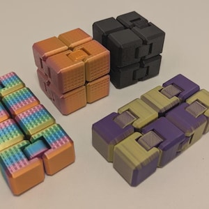 May include: Four fidget toys in various colors. One is rainbow-colored, another is orange, a third is black, and the last is purple and yellow. The toys are cube-shaped and designed to be manipulated.