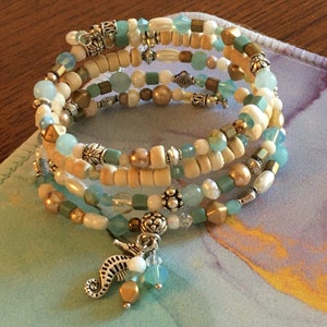 May include: A multi-strand bracelet with wooden beads, gold beads, and turquoise beads. The bracelet has a silver seahorse charm.