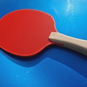 May include: A red ping pong paddle with a gray handle. The paddle has a textured surface and is set against a blue background. The handle has a curved design.