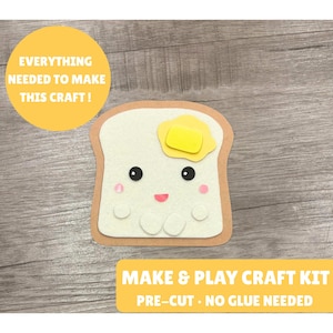 Puede incluir: Un kit de manualidades con una pieza de pan tostado con corteza marrón y centro blanco, coronada con un trozo de mantequilla amarillo. El pan tiene ojos negros, mejillas rosas y boca rosa. Texto: EVERYTHING NEEDED TO MAKE THIS CRAFT! MAKE & PLAY CRAFT KIT PRE-CUT • NO GLUE NEEDED