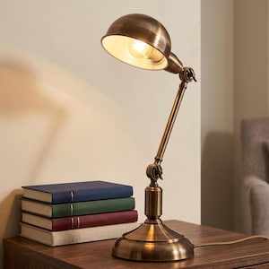 Brass reading lamp on a wooden desk beside stacked books in a cozy workspace