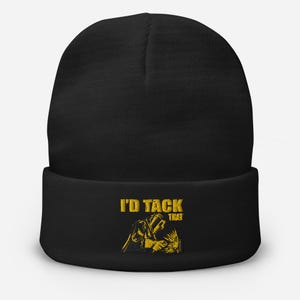 May include: Black beanie hat featuring the text "I'D TACK THAT" in gold. The design includes a gold illustration of a welder. A warm and comfortable hat for colder weather.