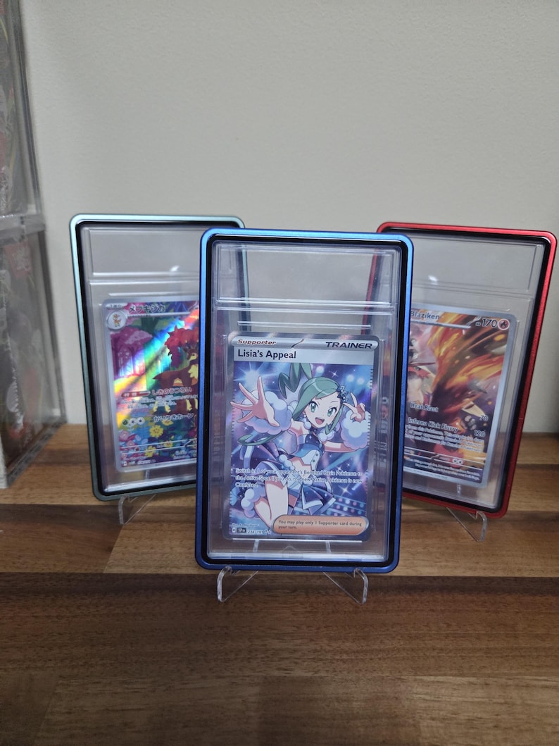 May include: Three trading cards in protective cases. The center card features a character named Lisia's Appeal, with the word "TRAINER" above the character. The cases have blue, red, and silver frames. The cards are displayed on clear stands.