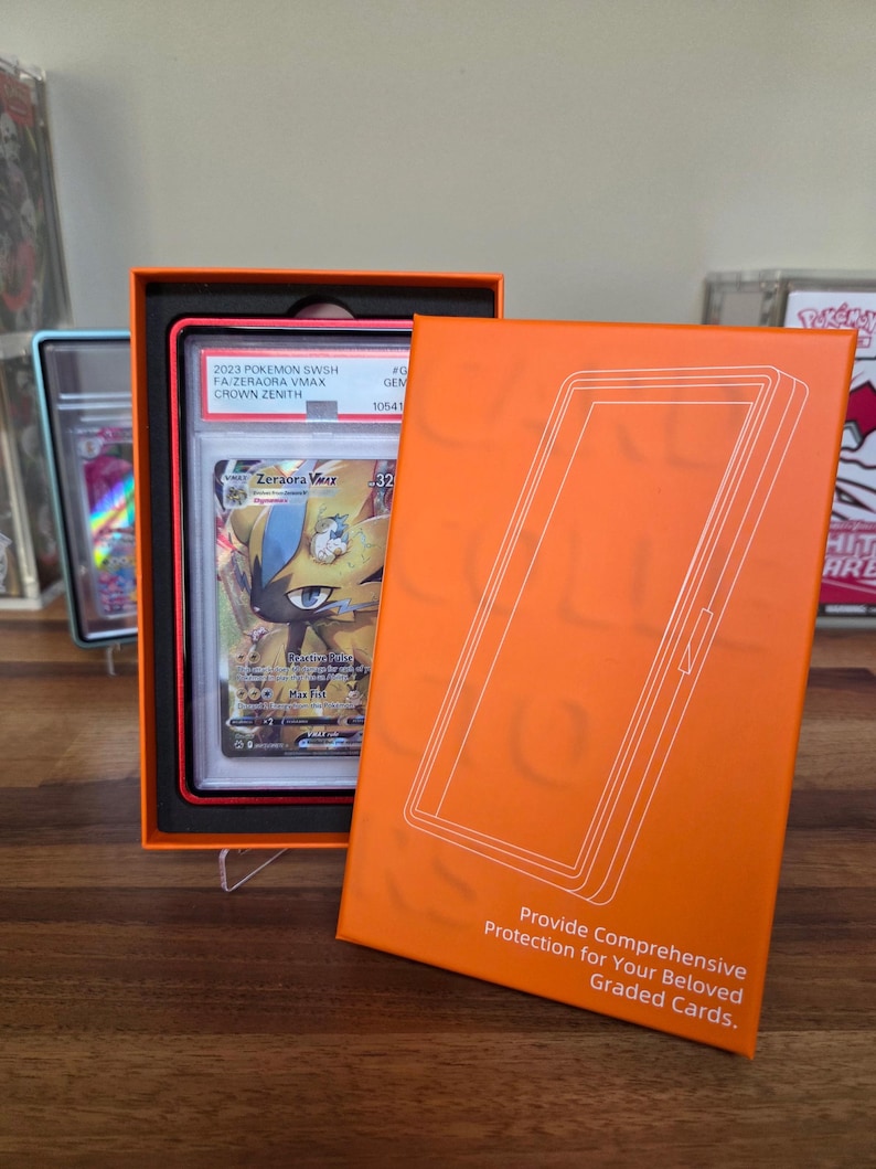 May include: An orange box with a graded Pok&eacute;mon card inside. The card features a Zeraora VMAX character. The box has the text "Provide Comprehensive Protection for Your Beloved Graded Cards."