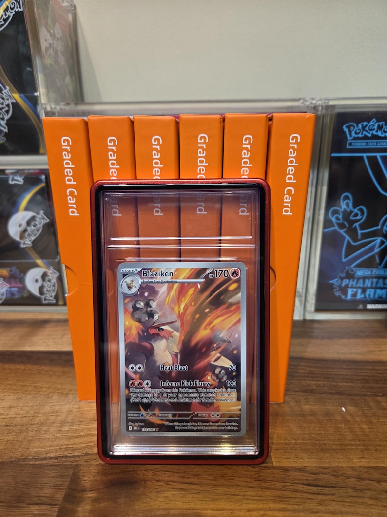 May include: A Blaziken Pok&eacute;mon card in a graded case, featuring a fiery illustration. The card is encased in a red-bordered holder, with orange graded card holders in the background. The card displays the text "Heat Blast" and "Inferno Kick Flurry".