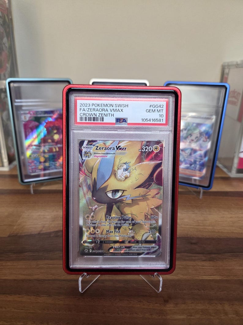 May include: A graded Pok&eacute;mon card featuring Zeraora VMAX from the Crown Zenith set. The card is encased in a red holder with the text "2023 POKEMON SWSH FA/ZERAORA VMAX CROWN ZENITH" and a grade of GEM MT 10. Other cards are visible in the background.