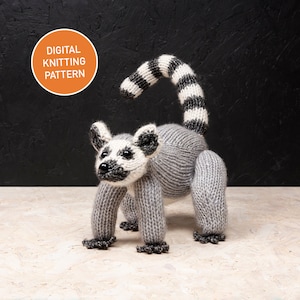May include: A knitted lemur toy in grey, white, and black, with a striped tail. The toy is standing on all fours. The image includes a circular orange graphic that says "DIGITAL KNITTING PATTERN".