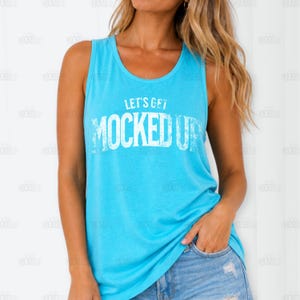 Puede incluir: Una camiseta sin mangas azul claro con el texto blanco "LET'S GET MOCKED UP". La camiseta sin mangas tiene cuello redondo y está hecha de un material suave. La modelo lleva pantalones cortos vaqueros.