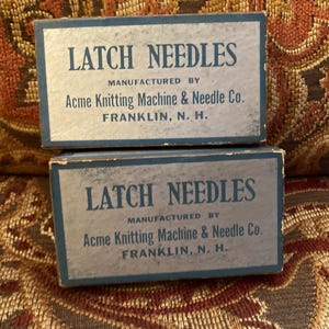 May include: Two rectangular light blue cardboard boxes stacked vertically, each labeled LATCH NEEDLES, MANUFACTURED BY Acme Knitting Machine & Needle Co. FRANKLIN, N. H. in dark blue text with a dark blue border around the edges.