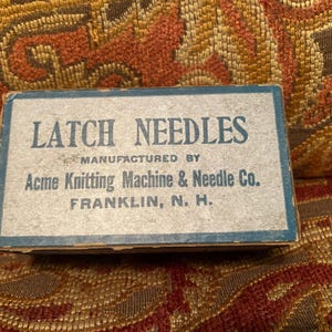 May include: A rectangular cardboard box for latch needles with a blue border and blue text that reads LATCH NEEDLES MANUFACTURED BY Acme Knitting Machine & Needle Co. FRANKLIN, N. H. The box has a light gray top surface.