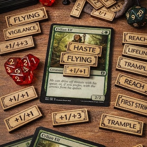 May include: Wooden game accessories, including dice, cards, and wooden tokens with game terms like "Flying" and "Trample." A "Cylian Elf" card is featured. Red dice and a small bag are also present.