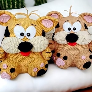 Op de afbeelding: Twee handgemaakte gehaakte tijgerknuffels. Eén is geel met zwarte vlekken, de andere is bruin met bruine vlekken. Beide hebben grote witte ogen, zwarte neuzen, roze oren en rode tongen. Ze zitten op een wit oppervlak.