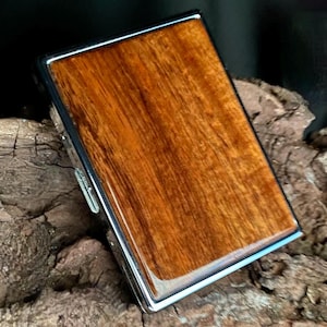 May include: A rectangular lighter with a polished, glossy wood grain finish. The lighter has a silver-colored metal frame and a hinged lid. The wood grain features shades of brown and reddish-brown.