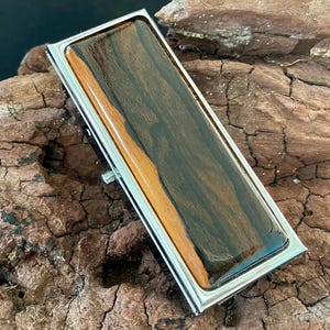 Peut inclure: Un porte-billets rectangulaire avec un cadre argenté poli. Le clip présente un centre en bois foncé avec un accent en bois plus clair. Le grain du bois est visible et ajoute un élément naturel au design.