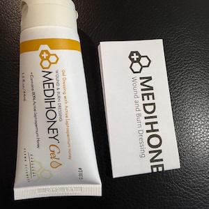 May include: A white tube of MEDIHONEY Gel wound and burn dressing with a yellow band and black text. A matching white card with the MEDIHONEY logo and text is next to the tube. The tube contains 1.5 fl. oz. / 44mL.