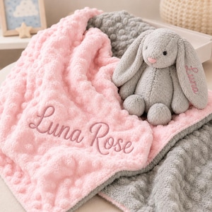 May include: A soft pink dimpled blanket with the name Luna Rose embroidered in dark pink thread, paired with a grey plush rabbit toy featuring long ears and the name Luna embroidered in matching pink thread on one of the rabbit's ears.