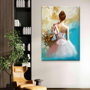 May include: A canvas art print depicts a ballerina in a pink and white tutu, holding ballet shoes. The painting has a teal and gold abstract background. The ballerina is facing away from the viewer. The artwork is displayed on a white wall.