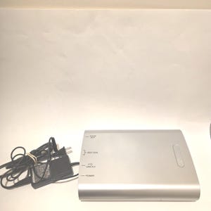 May include: Silver-colored electronic device with a power adapter and cord. The device has labeled ports for audio out, IEEE 1394, USB 2.0, and power. The power adapter is black.