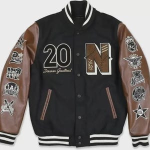 May include: Black varsity jacket with brown leather sleeves. Features the number "20" and the letter "N" with "1920" on the front. The jacket has multiple patches on the sleeves and the text "Discover Greatness".