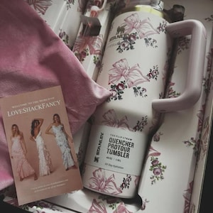 May include: A Stanley Quencher ProTour tumbler with a 40 oz capacity, featuring a white base with a pink floral and ribbon pattern, a light pink handle, and a matching straw, presented in a decorative box with a LoveShackFancy promotional card.