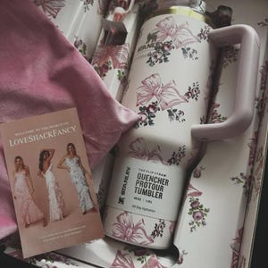 May include: A Stanley Quencher ProTour tumbler with a 40 oz capacity, featuring a white base with a pink floral and ribbon pattern, a light pink handle, and a matching straw, presented in a decorative box with a LoveShackFancy promotional card.