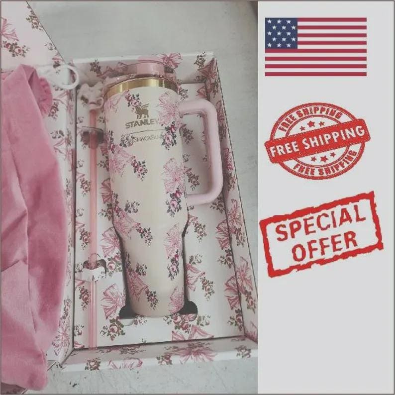 May include: A cream-colored Stanley tumbler with a floral pattern featuring pink and dark red flowers, a gold-tone rim, and a matching handle. The tumbler is presented in a box with a coordinating floral print, accompanied by a clear plastic straw.