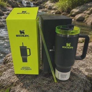 Puede incluir: Un vaso Stanley Quencher H2.0 negro mate con tapa y asa de color verde ne&oacute;n, acompa&ntilde;ado de una pajita verde ne&oacute;n a juego. El vaso se muestra junto a su caja de producto de color verde ne&oacute;n brillante y una caja negra, con el logotipo de Stanley.