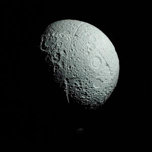 May include: A gray, spherical object with a textured surface, resembling a celestial body, is set against a black background. The object is segmented, with visible lines dividing its surface. The surface is covered in craters.