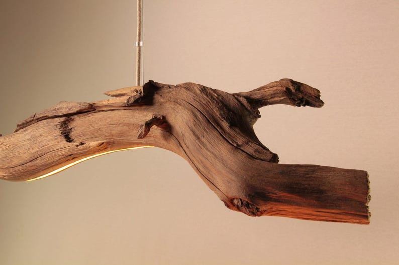 May include: A rustic, wooden pendant light fixture. The fixture is made from a natural, curved piece of driftwood, with a warm, glowing light emanating from the underside. The wood has a rich, brown color and visible grain.