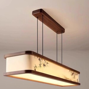 May include: Rectangular pendant light fixture with a wooden frame and a bamboo design on the shade. The light hangs from the ceiling by black cords. The fixture has a warm, inviting glow.