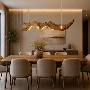 May include: A modern dining room featuring a long wooden table with eight beige chairs. Above the table hangs a unique, illuminated driftwood chandelier. The room has neutral tones, with a painting and a wooden cabinet in the background.