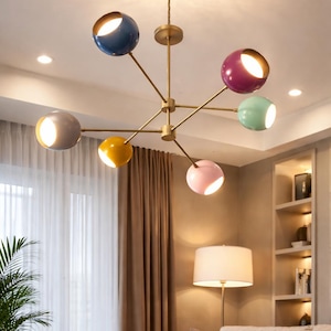 May include: A contemporary chandelier featuring a brass frame and seven spherical lampshades in various colours. The shades are blue, purple, green, grey, yellow, and pink. The light fixture is suspended from the ceiling.