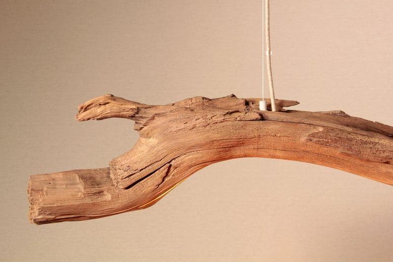 May include: A natural wood pendant light fixture. The fixture is made from a piece of driftwood, with a light-colored cord and a small, white fixture. The wood has a rough, textured surface and a warm, brown color.