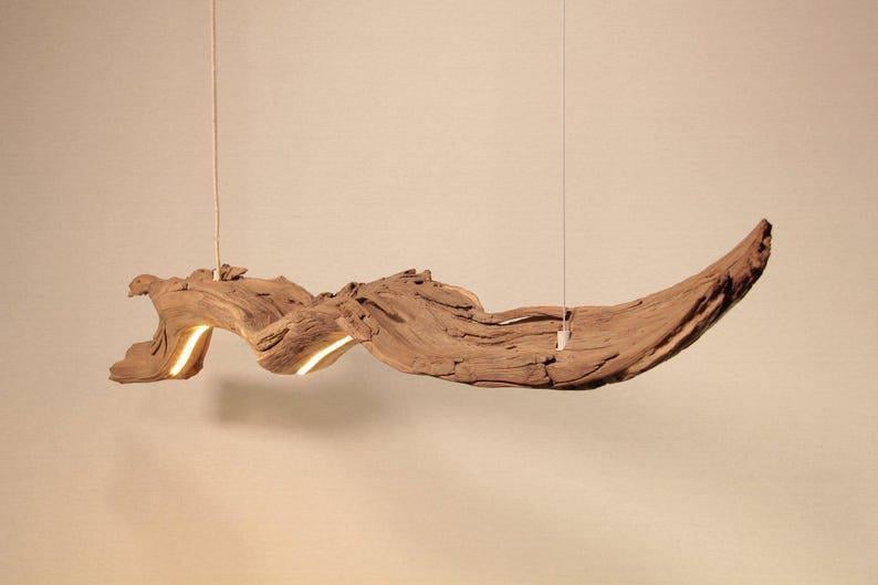 May include: A unique, handcrafted wooden pendant light fixture. The light is made from a natural piece of driftwood, with a warm, inviting glow emanating from within. The fixture hangs from a thin, nearly invisible cord.