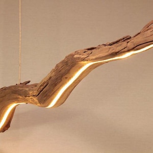 May include: A unique, handcrafted wooden pendant light fixture. The light is integrated into a natural, weathered driftwood branch, creating a warm, inviting glow. The fixture is suspended from the ceiling by a thin, neutral-colored cord, adding a touch of rustic elegance to any space.