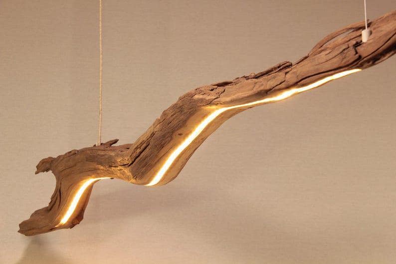 May include: A unique, handcrafted wooden pendant light fixture. The light is integrated into a natural, weathered driftwood branch, creating a warm, inviting glow. The fixture is suspended from the ceiling by a thin, neutral-colored cord, adding a touch of rustic elegance to any space.