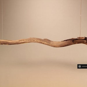 May include: A natural wood pendant light fixture. The light is suspended from a thin wire and features a long, curved, and textured wooden beam. The fixture includes a dimmer and power button.