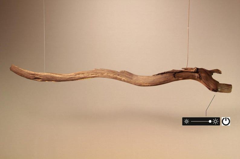 May include: A natural wood pendant light fixture. The light is suspended from a thin wire and features a long, curved, and textured wooden beam. The fixture includes a dimmer and power button.